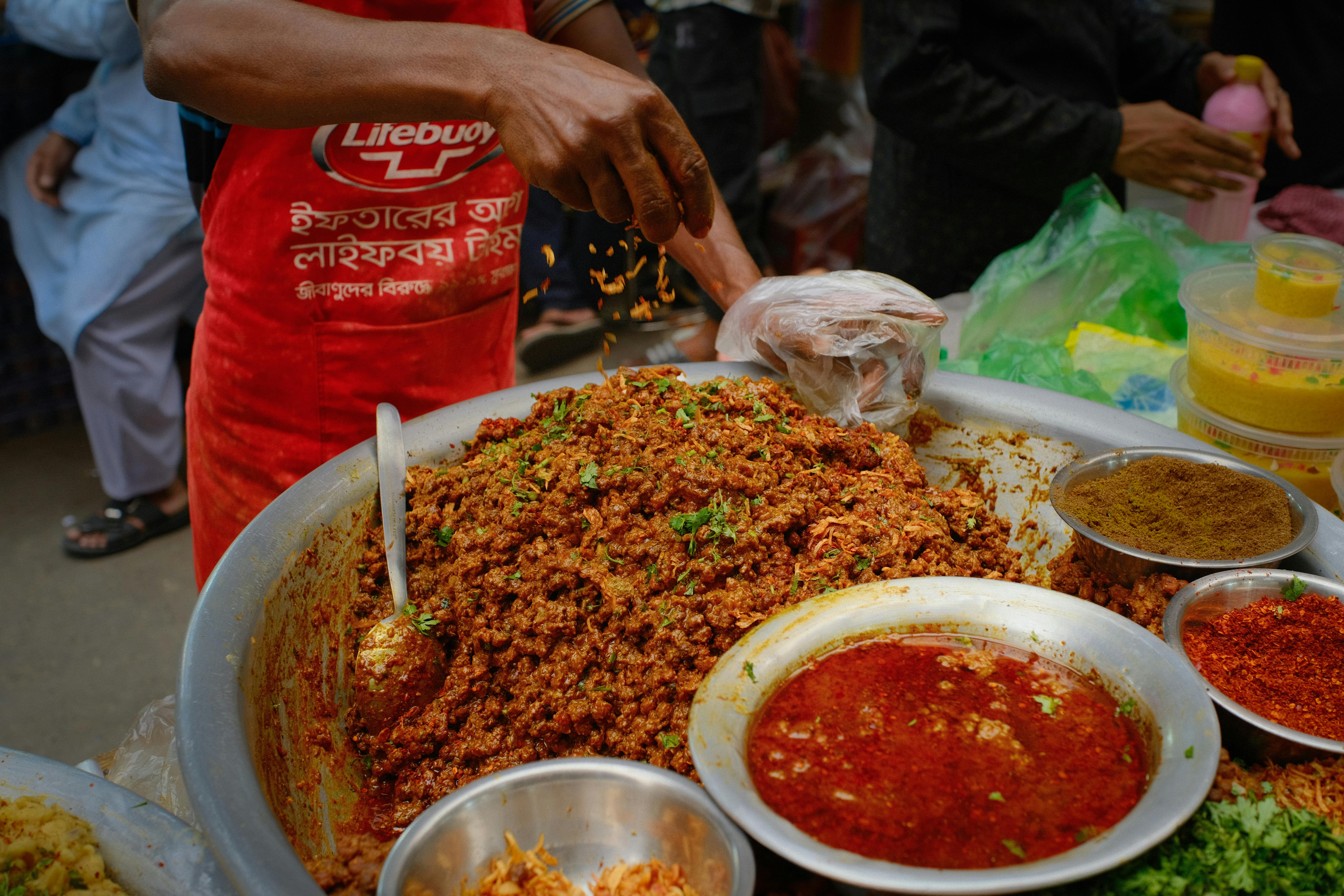 Colorful street food being prepared at a bustling Dhaka iftar market during Ramadan.